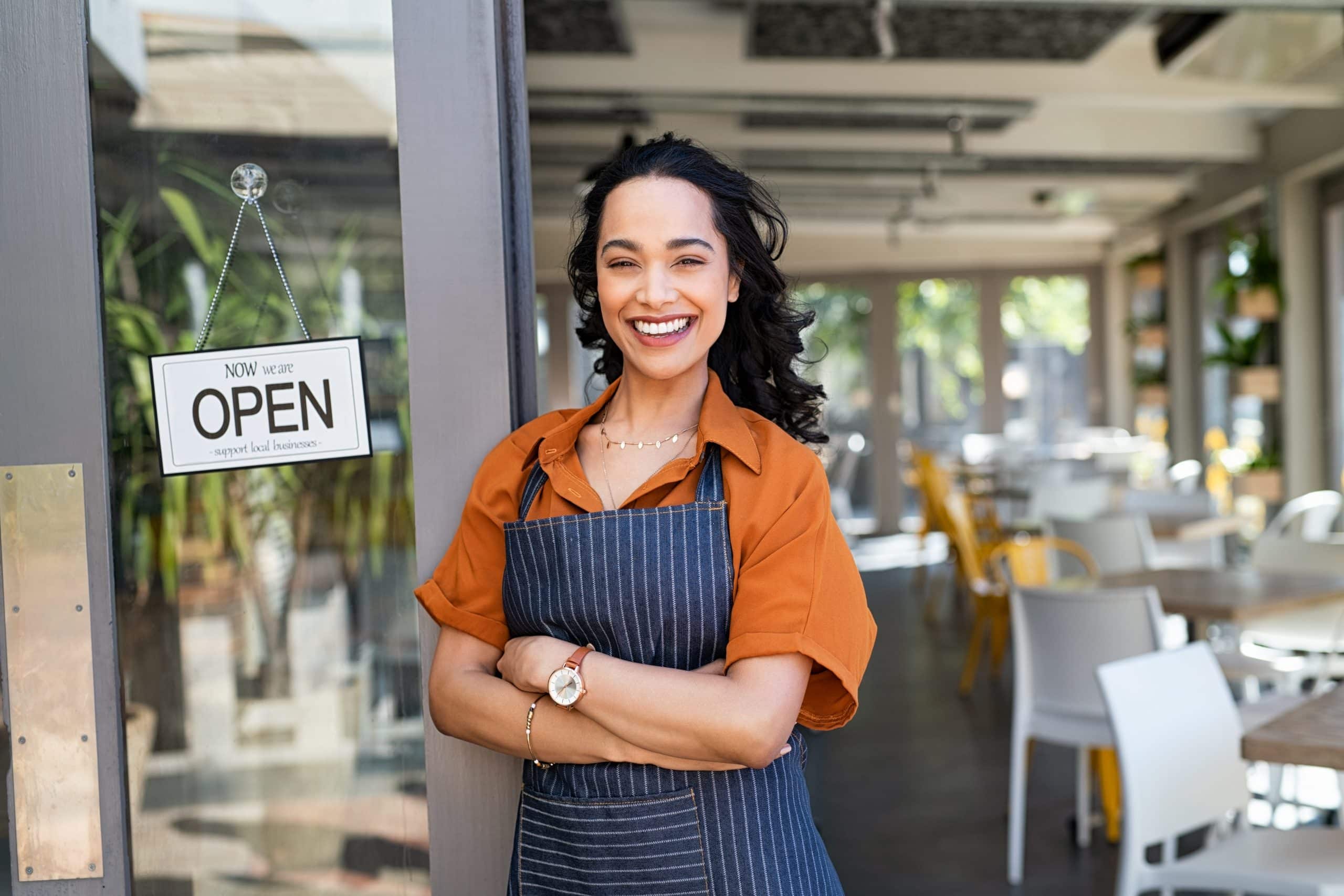 Young business woman wearing apron standing with open sign at entrance gate